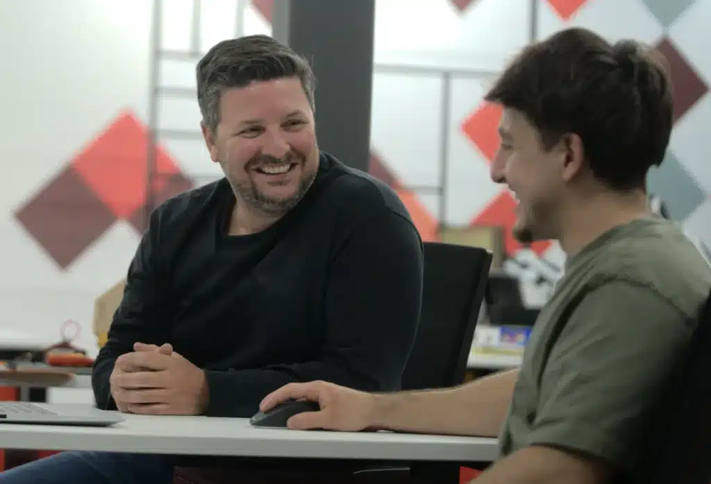 Deux collègues souriants qui discutent à une table de travail dans un bureau moderne